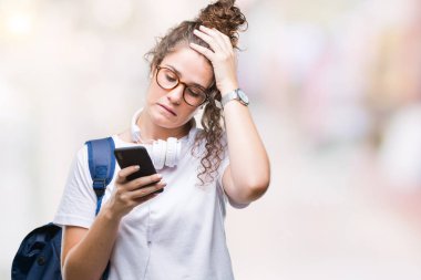 Genç esmer öğrenci kız giyiyor sırt çantası, kulaklık ve akıllı telefon başında, utanç ve sürpriz ile şok el ile vurguladı izole arka plan üzerinde yüz, öfkeli ve sinirli. Korku ve hata için üzgün.