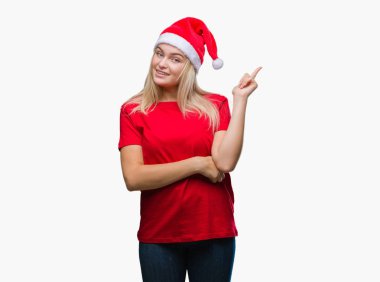 Kameraya bakarak yan el ve parmak ile işaret yüzünde kocaman bir gülümseme ile izole arka plan üzerinde Noel şapka giyen genç beyaz kadın.