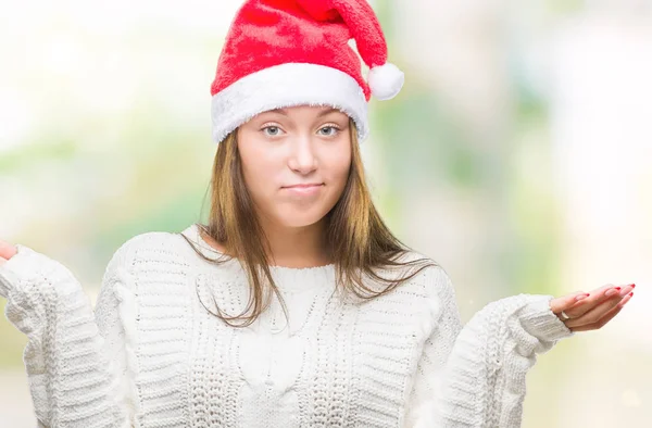 年轻美丽的白人妇女戴着圣诞帽子在孤立的背景下没有头绪和混淆的表达与胳膊和手提出 怀疑概念 — 图库照片
