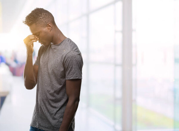 Молодой африканский американец в серой футболке устал тереть нос и глаза, чувствуя усталость и головную боль. Концепция стресса и разочарования
.