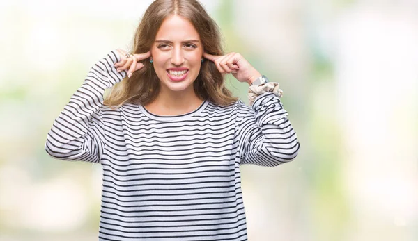 騒々しい音楽のノイズの腹式指で耳を覆う孤立の背景の上のストライプのセーターを着て美しい若い金髪女性 聴覚障害者の概念 — ストック写真