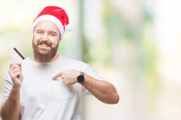 自分自身に驚き顔ポインティング指で孤立した背景の上クレジット カードを保持しているクリスマスの帽子を身に着けている若い白人男 — ストック写真