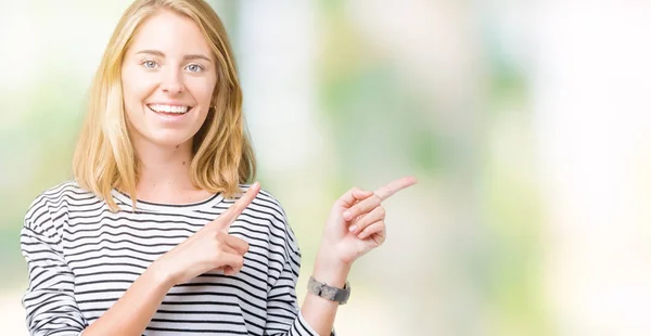 笑顔で側に つの手と指で指しているカメラを見て孤立の背景の上のストライプのセーターを着て美しい若い女性 — ストック写真