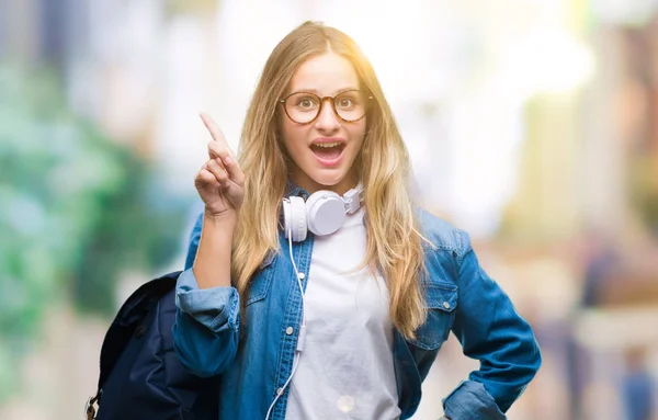 分離背景人差し指の上のヘッドフォンとメガネを成功したアイデアを着て若い美しい金髪学生女性 終了したと満足しています ナンバーワン — ストック写真