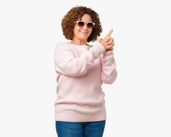 美しい中間エイガー年配の女性にピンクのセーター サングラスを着て分離背景手ジェスチャーで象徴的な銃を保持している 射撃武器 怒った顔を殺して遊んで — ストック写真
