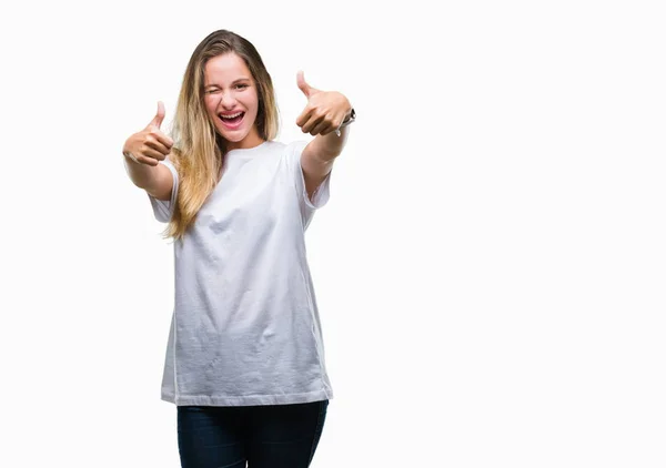 年轻美丽的金发女子穿着休闲白色 T恤在孤立的背景批准做积极的手势与手 竖起大拇指微笑和快乐的成功 看着相机 赢家手势 — 图库照片