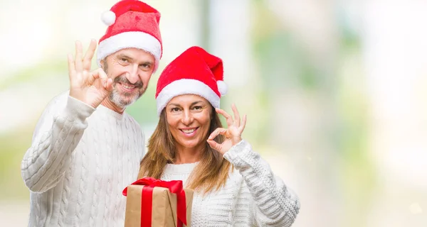 優秀なシンボルの指で サインをして孤立した背景の上身に着けているクリスマスの帽子 持株ギフト中年ヒスパニック系カップル — ストック写真