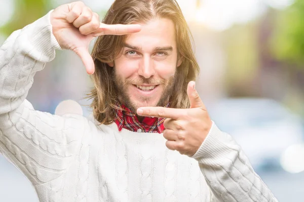 笑顔の幸せそうな顔で指と手作りフレーム分離の背景に冬のセーターを着ている髪の長い若いハンサムな男 創造性と写真のコンセプト — ストック写真