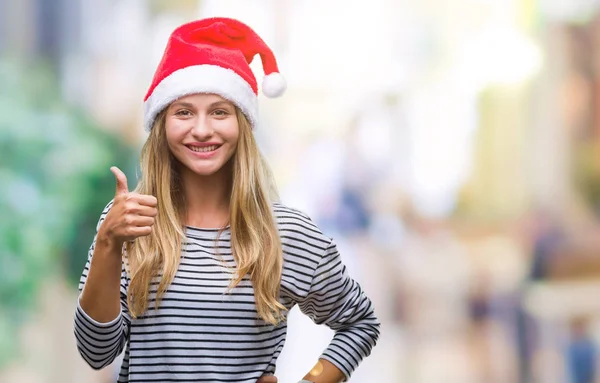 若い美しい金髪女性のハッピー サムズアップ手でジェスチャーをして孤立した背景にクリスマス帽子をかぶっています 成功を示すと カメラを見て式を承認します — ストック写真