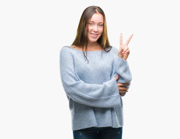 勝利のサインを行うカメラでウィンクしている幸せそうな顔を浮かべて隔離された背景に冬のセーターを着た若い美しい白人女性 — ストック写真