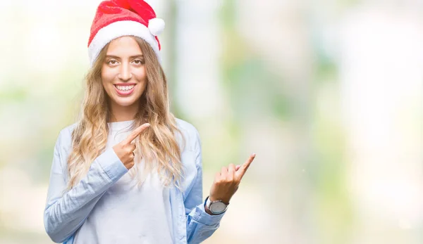 分離背景笑顔で側に つの手と指で指しているカメラ目線の上クリスマス帽子身に着けている美しい若いブロンドの女性 — ストック写真