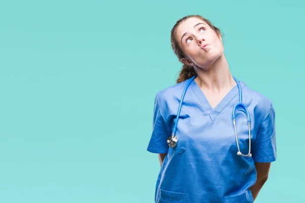Young brunette doctor girl wearing nurse or surgeon uniform over isolated background making fish face with lips, crazy and comical gesture. Funny expression.