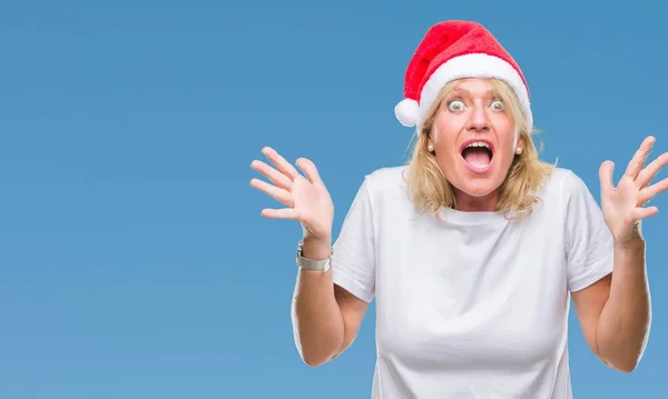 Middle age blonde woman wearing christmas hat over isolated background celebrating crazy and amazed for success with arms raised and open eyes screaming excited. Winner concept