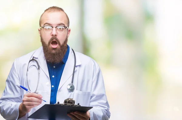 Young doctor man holding clipboard over isolated background scared in shock with a surprise face, afraid and excited with fear expression