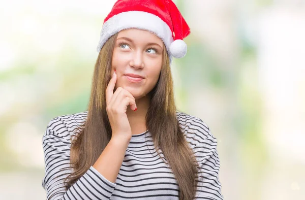 若い美しい白人女性のあごを考えて質問 物思いにふける式の手で隔離された背景にクリスマス帽子をかぶっています 思いやりのある顔をして笑っています 疑いのコンセプト — ストック写真