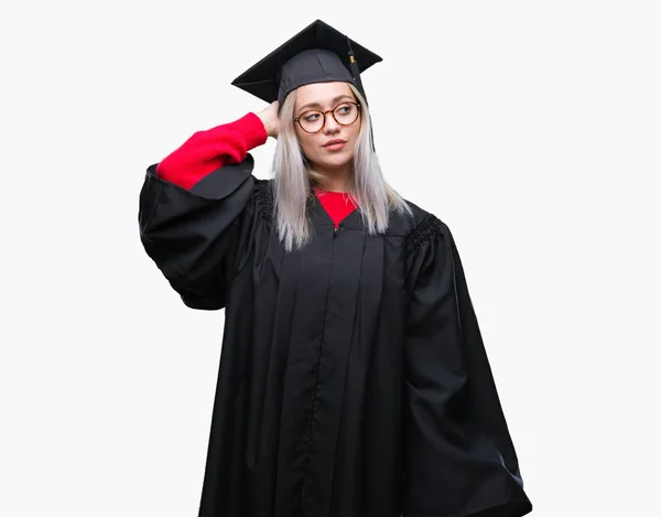 年轻的金发女子穿毕业制服在孤立的背景混淆和疑惑的问题 疑惑不定 用手在头上思考 沉思概念 — 图库照片