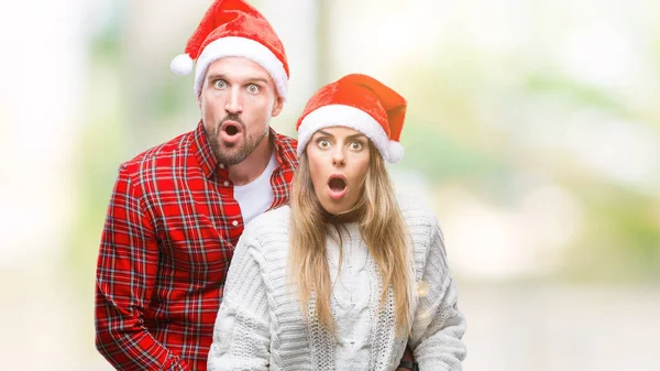 驚きの表現 恐怖と興奮した顔でショックを受けて孤立した背景にクリスマスの帽子をかぶっての愛の若いカップル — ストック写真