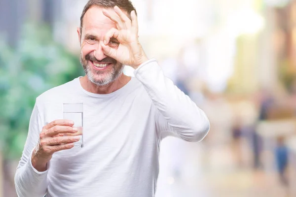 指の間から見て目に手で サインをして笑っている幸せそうな顔で孤立した背景に水のガラスを飲む中年白髪年配の男性 — ストック写真