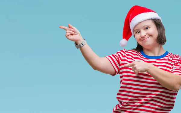 有唐氏综合症的年轻成年妇女戴着圣诞帽在与世隔绝的背景下微笑着 看着两只手和手指指向侧面的相机 — 图库照片