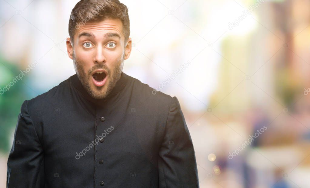 Young catholic christian priest man over isolated background afraid and shocked with surprise expression, fear and excited face.