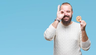Genç hipster man ile mutlu yüz el parmaklarının arasından seyir göz üzerinde ok işaretiyle yapıyor gülümseyen izole arka plan üzerinde çikolata çerez yemek