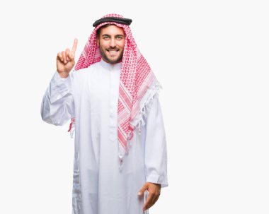 Keffiyeh ve parmak gülümseyen süre bir numara ile kendinden emin ve mutlu yukarıyı gösteren izole arka plan üzerinde giyen genç yakışıklı adam.