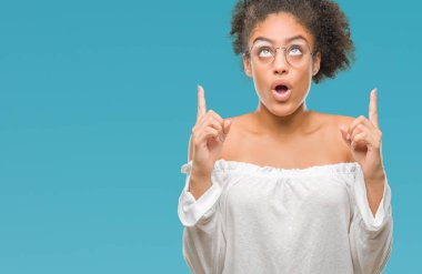Genç afro Amerikalı kadın hayrete ve yukarıya bakıyor ve parmakları ile işaret ve silah kaldırdı sürpriz izole arka plan üzerinde gözlük.