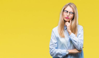 Genç güzel sarışın iş kadın gözlük ile izole arka plan üzerinde çene düşünme hakkında soru, dalgın ifade ver. Düşünceli yüzüyle gülümsüyor. Şüphe kavramı.