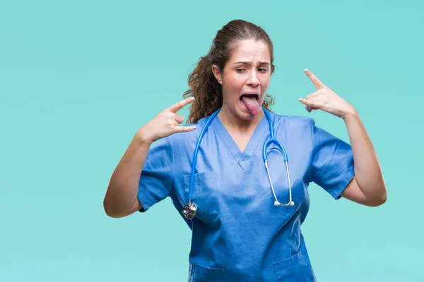 Young brunette doctor girl wearing nurse or surgeon uniform over isolated background shouting with crazy expression doing rock symbol with hands up. Music star. Heavy concept.