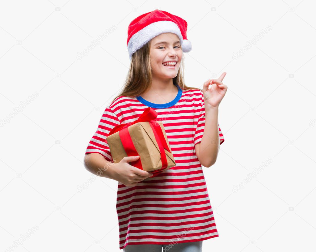 Young beautiful girl wearing christmas hat and holding gift over isolated background very happy pointing with hand and finger to the side