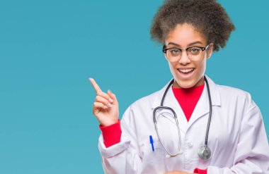 Kameraya bakarak yan el ve parmak ile işaret eden genç afro Amerikalı doktor kadın yüzünde kocaman bir gülümseme ile izole arka plan üzerinde.