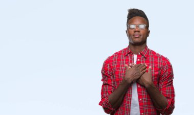 Göğüs kapalı gözler ve yüzünde minnettar jest ile genç Afro-Amerikan adam ile gülümseyen izole arka plan üzerinde eller. Sağlık kavramı.