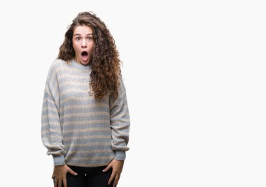 Güzel esmer kıvırcık saçlı Genç kız korkuyor ve şok sürpriz ifade, korku ve heyecan yüz ile izole arka plan üzerinde kış kazak giyiyor.