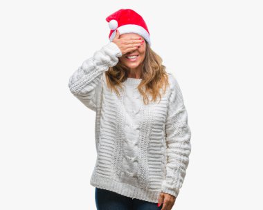 Orta yaş üst düzey İspanyol kadın gülümsüyor ve gözleri için sürpriz kapsayan yüz el ile gülüyor izole arka plan üzerinde Noel şapka giyiyor. Kör kavramı.