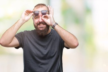 Genç beyaz hipster adam gülümsüyor, parmakları ile mutlu yüz üzerinden seyir göz el ile ok jest yapıyor izole arka plan üzerinde güneş gözlüğü takıyor.