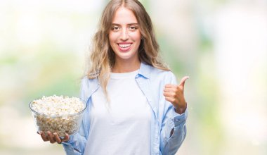 Ok işareti, başparmak ile parmak, mükemmel işareti yapıyor kocaman bir gülümseme ile izole arka plan üzerinde mutlu patlamış mısır yemek güzel sarışın genç kadın