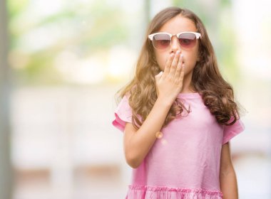 Esmer Latin kız giyiyor güneş gözlüğü kapak ağız el için hata, ifade korku, utanç ile şok ile sessizlik içinde gizli kavramı korkuttu