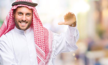 Keffiyeh ile büyük ve büyük boy işaret, ölçü birimi sembol gösteren el eller izole arka plan üzerinde giyen genç yakışıklı adam. Kameraya bakarak gülümsüyordu. Ölçüm kavramı.