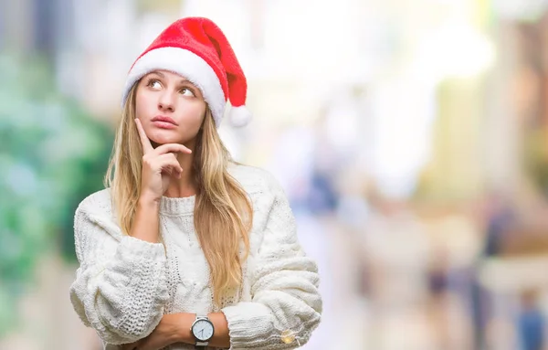 若い美しい金髪女性のあごを考えて質問 物思いにふける式の手で隔離された背景にクリスマス帽子をかぶっています 思いやりのある顔をして笑っています 疑いのコンセプト — ストック写真