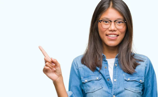 カメラを見て側に手と指で指している眼鏡の顔に大きな笑みを浮かべて隔離された背景に若いアジア女性 — ストック写真