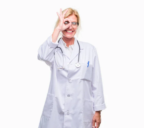 中年金发医生妇女在孤立的背景下做 手势用手微笑 眼睛看通过手指与愉快的面孔 — 图库照片