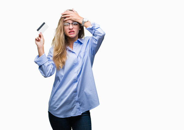 Young beautiful blonde woman holding credit card over isolated background stressed with hand on head, shocked with shame and surprise face, angry and frustrated. Fear and upset for mistake.