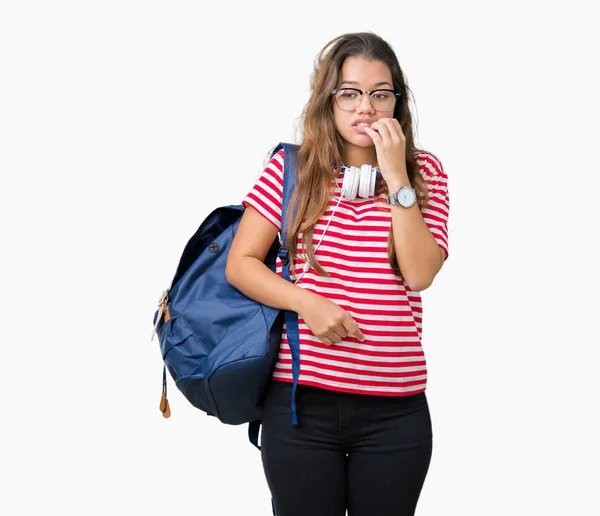 美しいブルネットの学生の若い女性は不安や両手の爪を噛んで口の中で緊張を探して孤立の背景にヘッドフォンとバックパックを着用します 不安の問題 — ストック写真