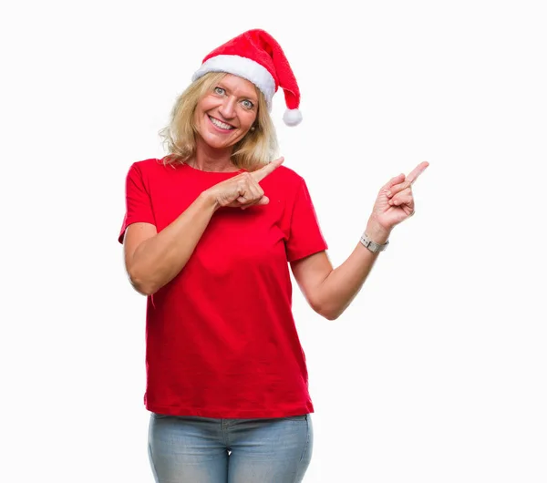 中年金发女子戴着圣诞节帽子在孤立的背景微笑和看着相机指着两个手和手指到一边 — 图库照片