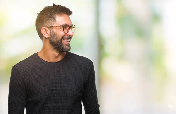 Adult hispanic man wearing glasses over isolated background looking away to side with smile on face, natural expression. Laughing confident.