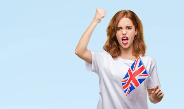 年轻美丽的妇女持有英国国旗在孤立的背景恼怒和沮丧的呼喊与愤怒 疯狂和叫喊与举手 愤怒的概念 — 图库照片