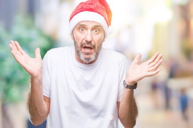 İzole arka plan clueless ve şaşkın bir ifadeyle kollar ve eller kaldırdı üzerinde Noel şapka orta yaş ağarmış komuta sizde. Şüphe kavramı.