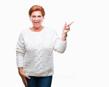 Kameraya bakarak yan el ve parmak ile işaret yüzünde kocaman bir gülümseme ile izole arka plan üzerinde kış kazak giyen Atrractive üst düzey beyaz Kızıl saçlı kadın.