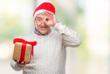 Üst düzey yakışıklı Noel şapka ve holding hediye ile mutlu yüz el parmaklarının arasından seyir göz üzerinde ok işaretiyle yapıyor gülümseyen izole arka plan üzerinde giyen