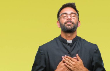 Yetişkin İspanyol göğüs kapalı gözler ve yüzünde minnettar jest ile Katolik rahip adam ile gülümseyen izole arka plan üzerinde eller. Sağlık kavramı.